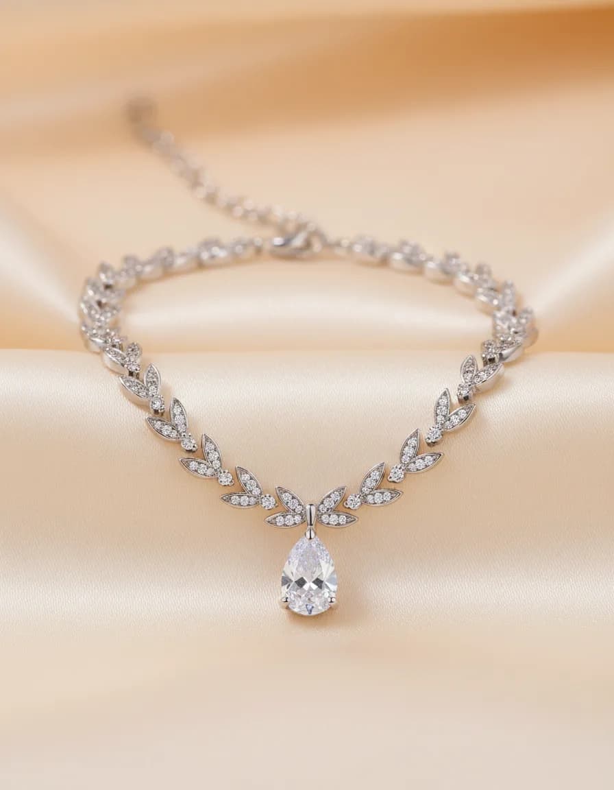 Collar plateado de brillantes en forma de hojas con una gota central, sobre tela de satín marfil